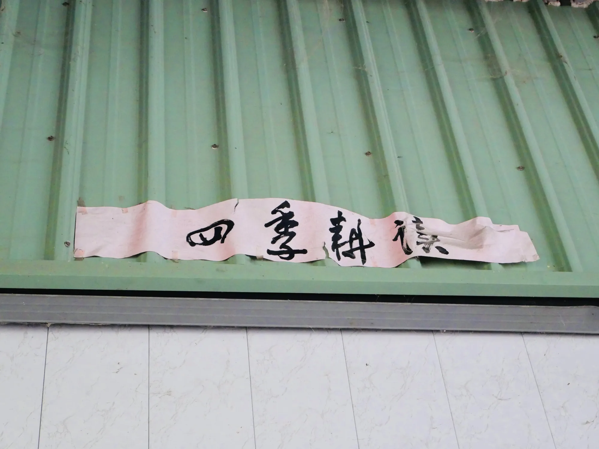 綠色鐵皮牆上貼著手寫的四季耕讀四個字