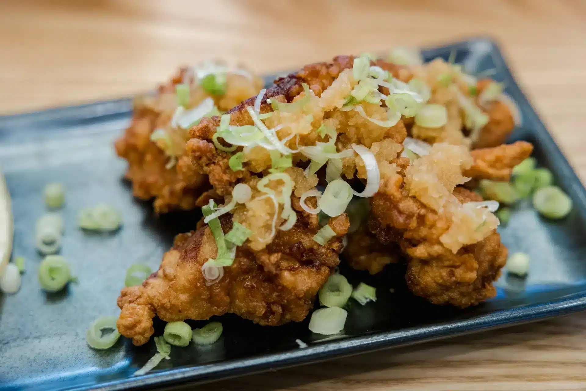 日式炸雞から揚げ成品特寫,金黃酥脆的雞塊鋪上蔥花與蘿蔔泥盛在藍色方盤上