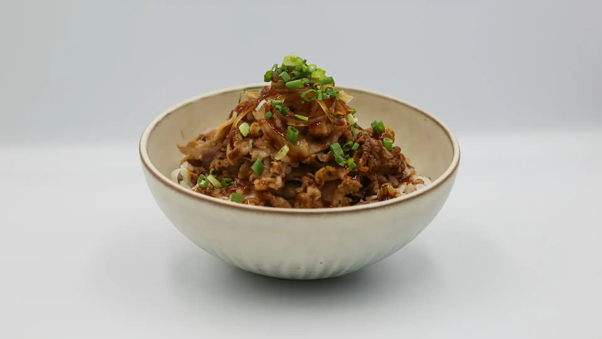 日式牛丼盛在陶碗裡,鹹甜醬汁的牛肉片與洋蔥鋪在白飯上,撒上蔥花