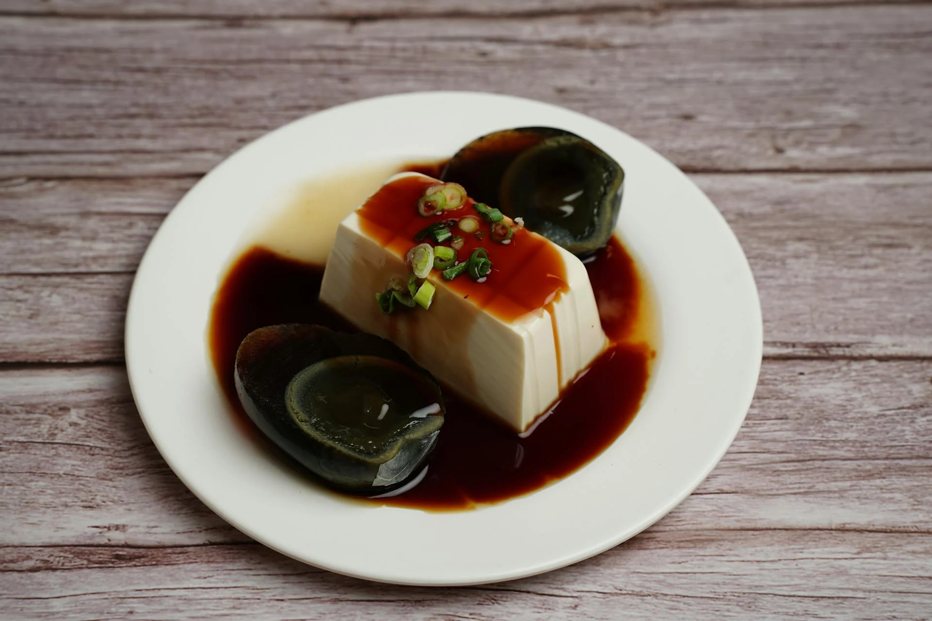 日照糙米油膏淋在皮蛋豆腐上的特寫,白瓷盤裝、蔥花點綴、油膏深褐釉亮