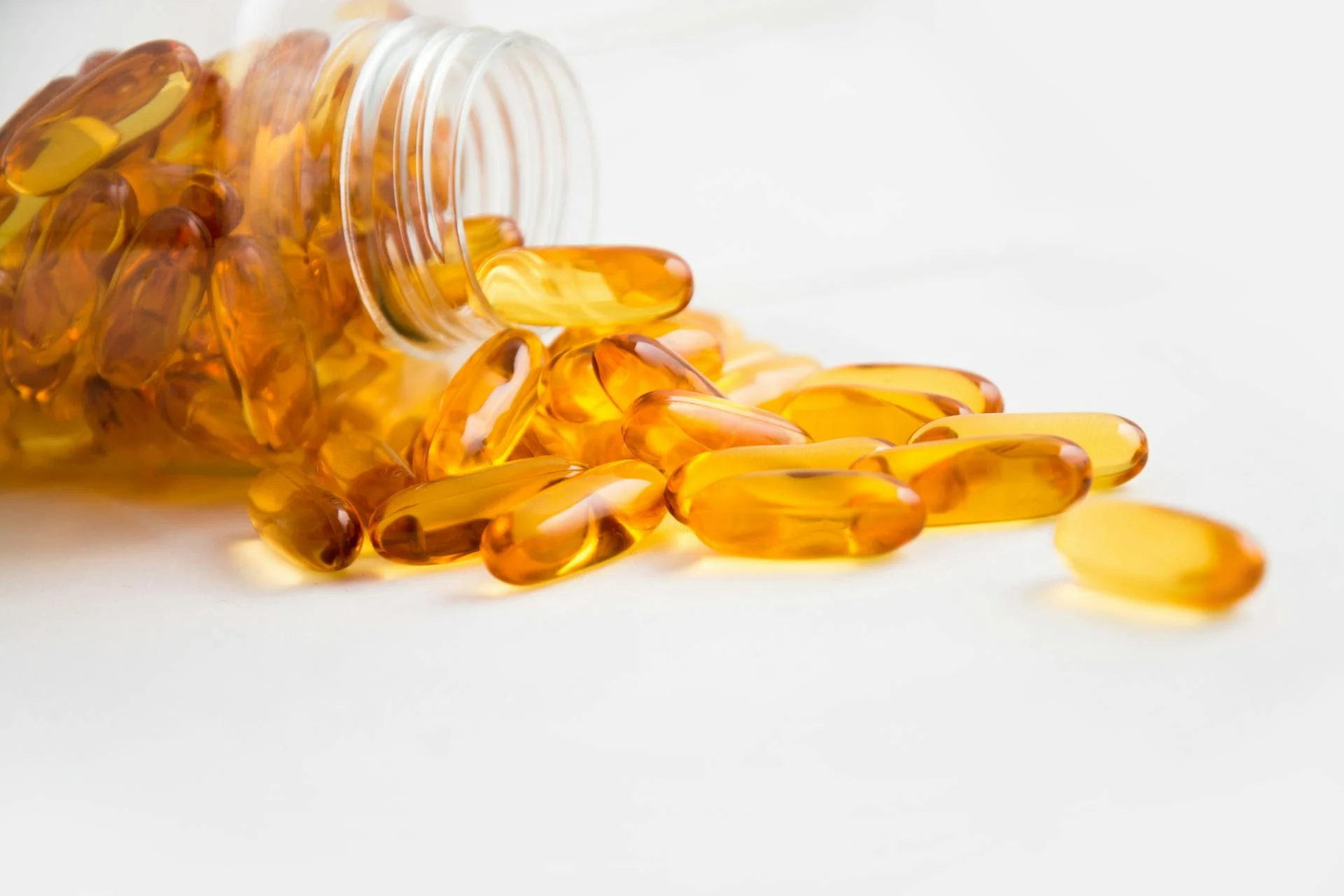 魚油 Omega-3 膠囊從玻璃瓶倒出散在白色桌面上，傳統 Omega-3 補充來源的形象