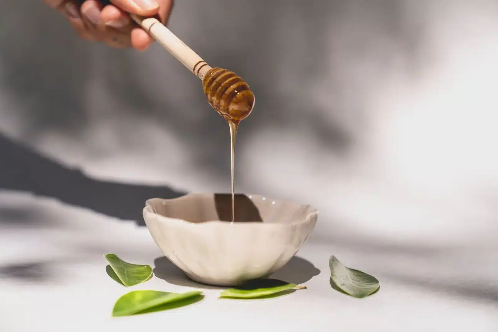 蜂蜜從木製沾蜜棒緩緩流入陶碗，金黃濃稠展現天然蜂蜜的質地與光澤