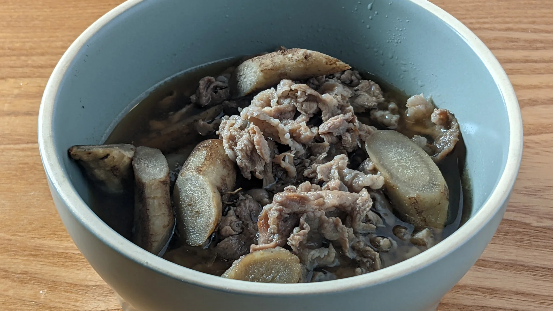 碗裡煮透的牛蒡厚斜片與豬肉片，牛蒡邊緣的皮仍在，湯色深褐帶著光澤