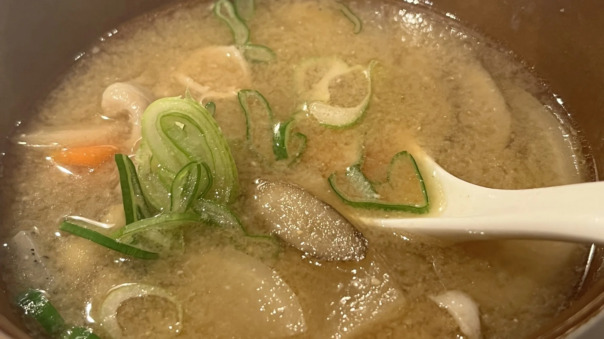 一碗加了牛蒡片、紅蘿蔔與蔥花的味噌湯，湯匙正舀起一片煮軟的牛蒡斜片