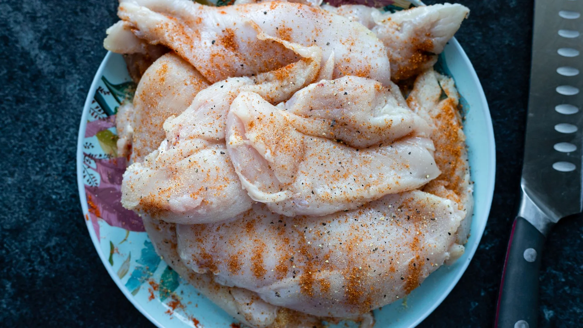 調味過的生雞胸肉盛在盤中，旁邊放著刀