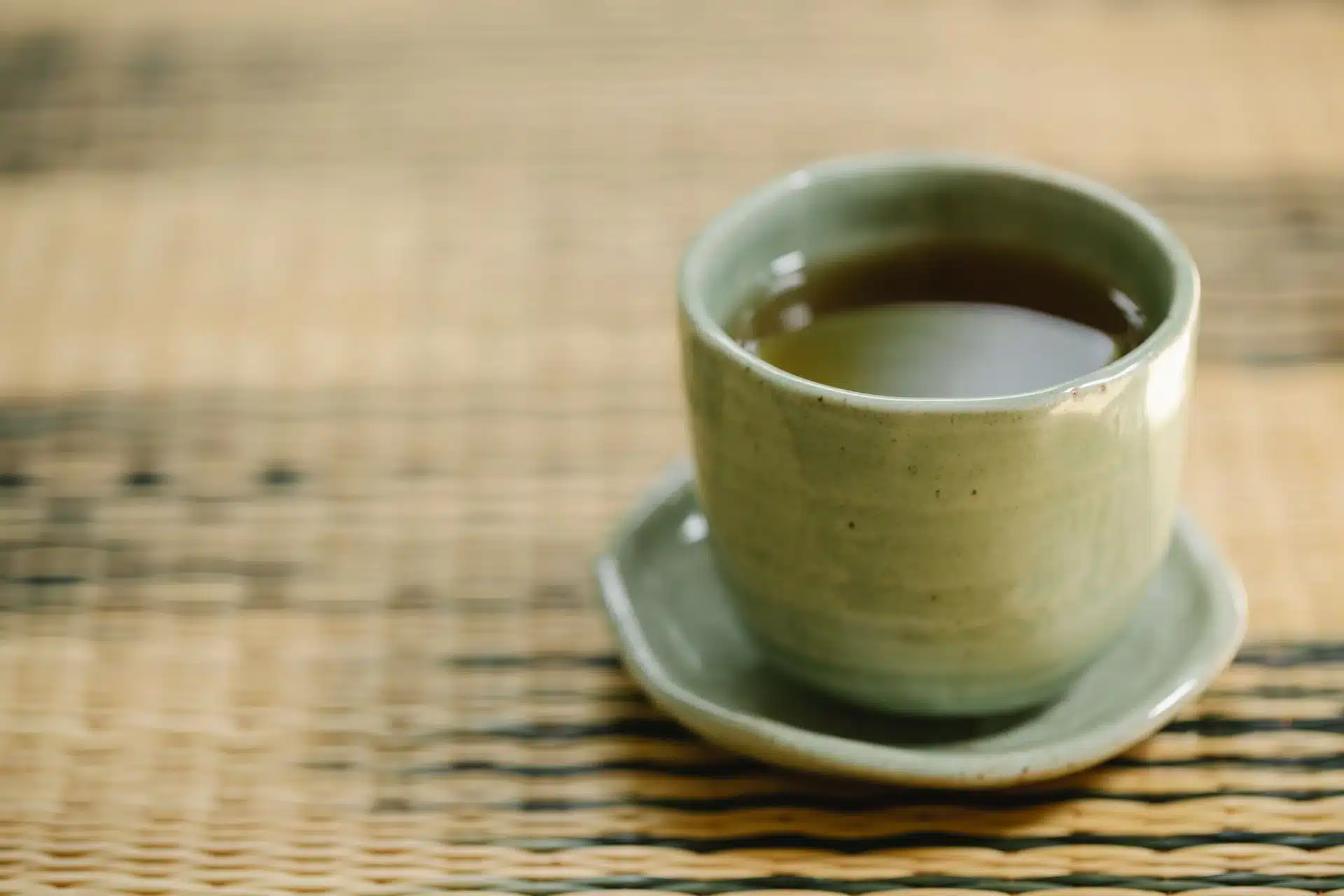 日式陶杯裝著焙茶色的玄米茶，放在編織茶席上透著暖光