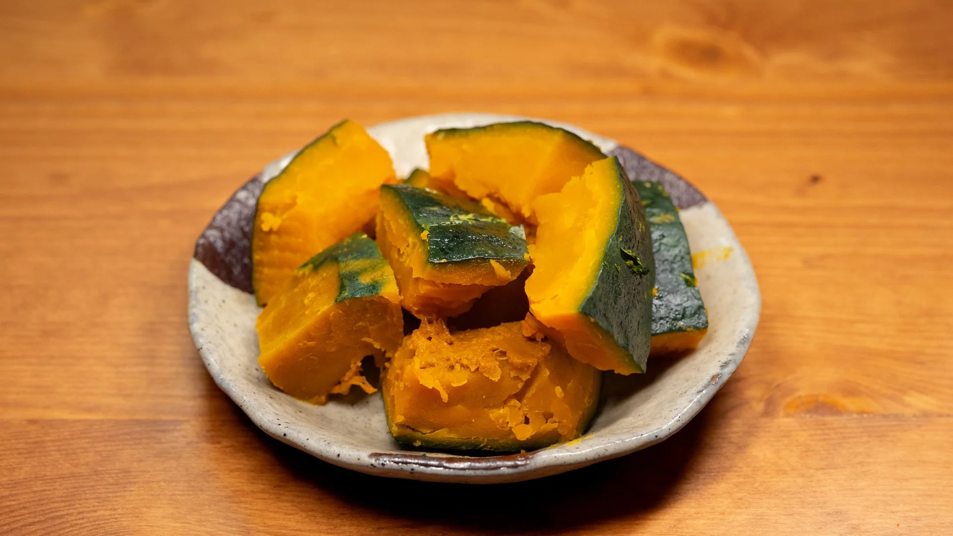 日式陶盤上蒸好的南瓜塊，墨綠色的皮還留著，果肉是深橘黃色