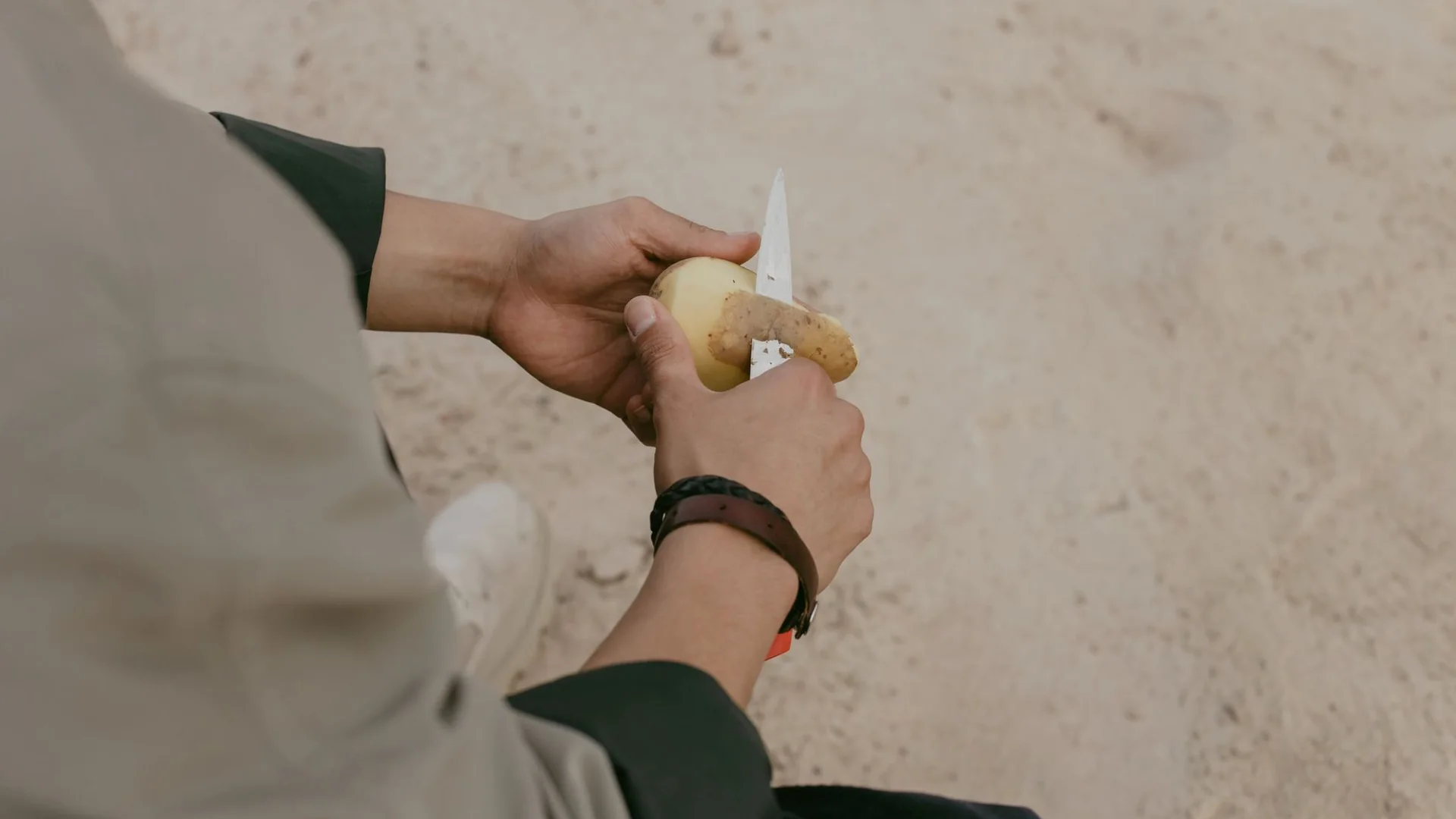 手持小刀削去根莖類食材外皮的特寫，削芋頭時建議戴手套或保持乾手