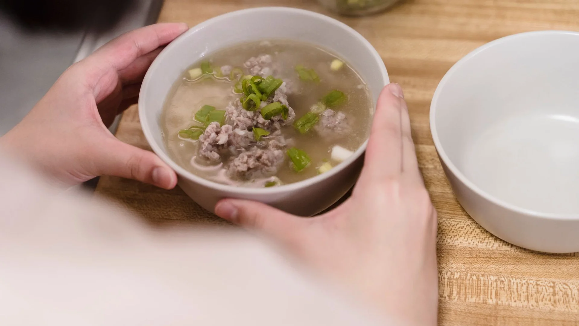 雙手捧著一碗清澈的排骨湯，湯裡有肉末與蔥花，呈現家常山藥排骨湯的日常樣貌