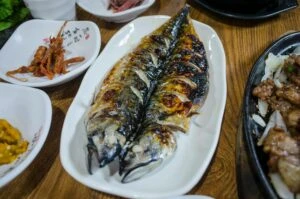 烤鯖魚裝以白盤隨以韓式側菜，omega3 魚類來源代表